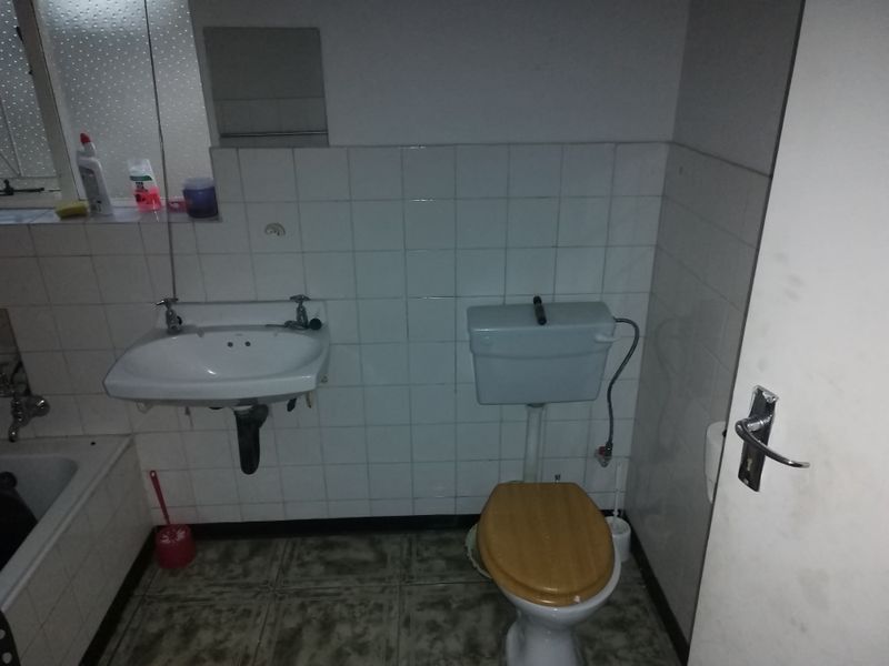 A dated bathroom featuring a wall-mounted basin, toilet, and bathtub with tiled finishes, requiring modernization to improve functionality and aesthetic appeal.