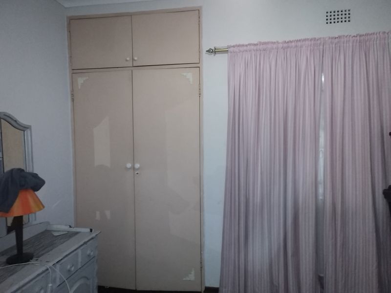 A bedroom featuring a built-in wardrobe with overhead storage and a ventilation grille, showing signs of wear on the cabinetry finish.