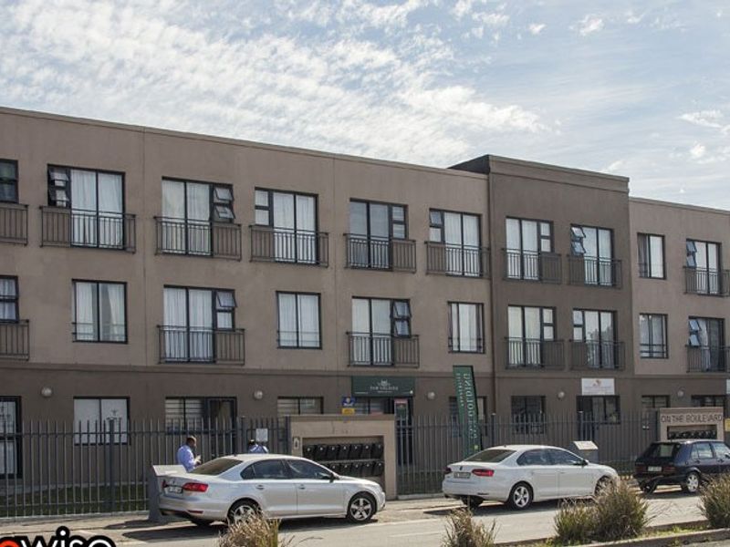 Front elevation of a multi-story apartment complex featuring modern facade, metal security fencing, and individual balconies for each unit.