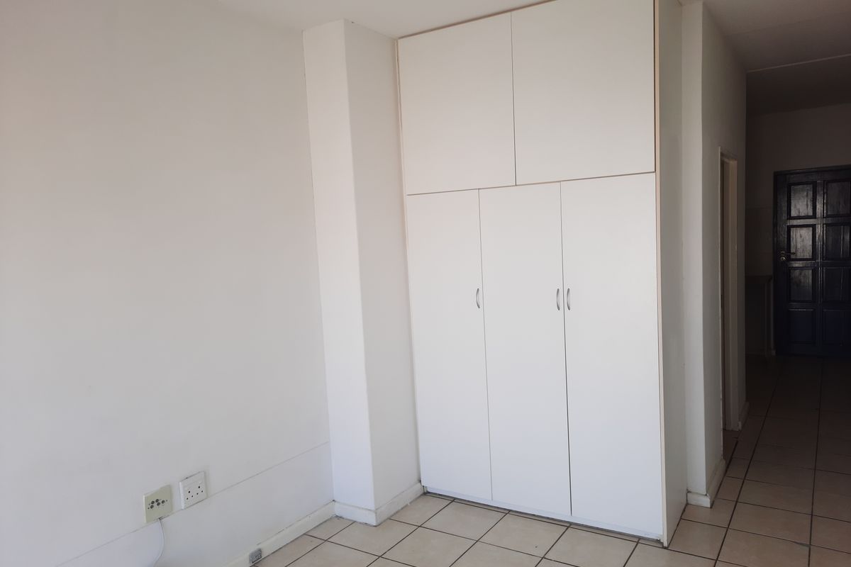 A clean, empty bedroom featuring white built-in cupboards and neutral tiled flooring, offering a blank canvas for personalization.