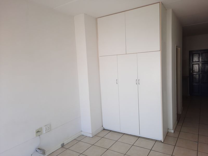 A clean, empty bedroom featuring white built-in cupboards and neutral tiled flooring, offering a blank canvas for personalization.