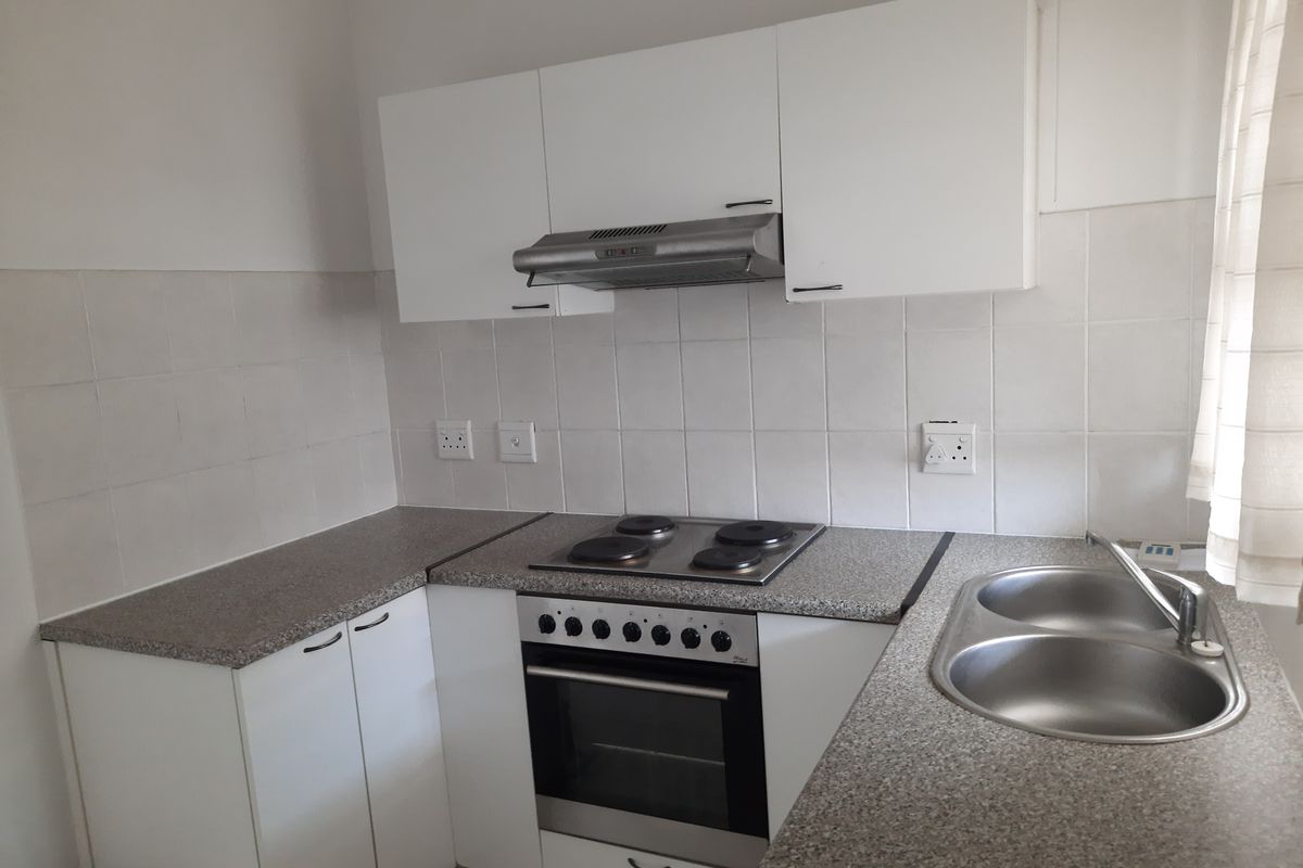 A functional kitchen featuring white cabinetry, laminate countertops, a stainless steel double sink, and built-in electric cooking appliances with a tiled splashback.