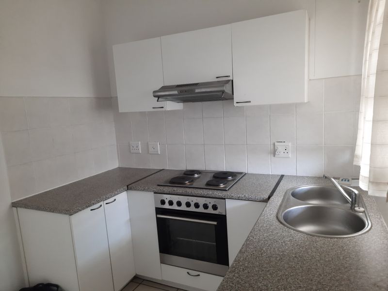A functional kitchen featuring white cabinetry, laminate countertops, a stainless steel double sink, and built-in electric cooking appliances with a tiled splashback.