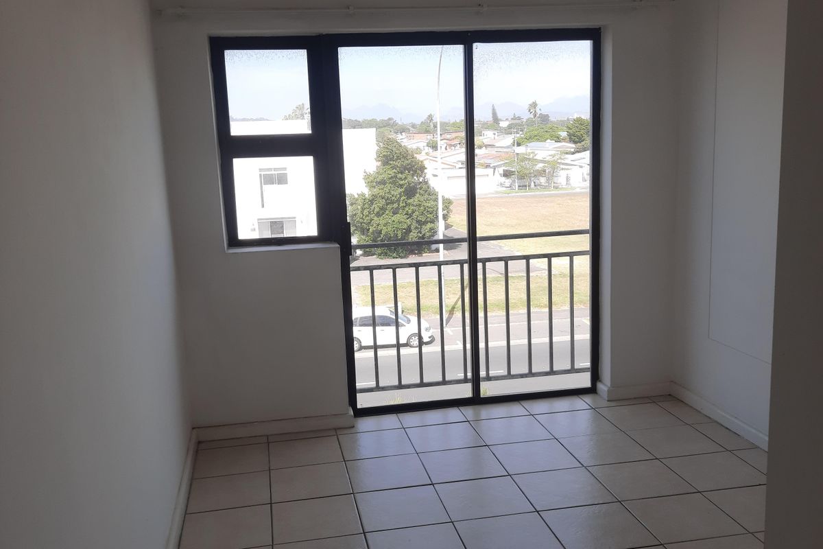 An empty bedroom featuring tiled flooring and a sliding glass door that opens onto a balcony with exterior views.