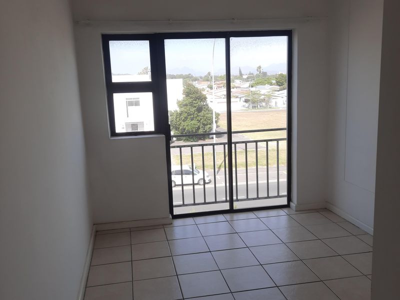 An empty bedroom featuring tiled flooring and a sliding glass door that opens onto a balcony with exterior views.