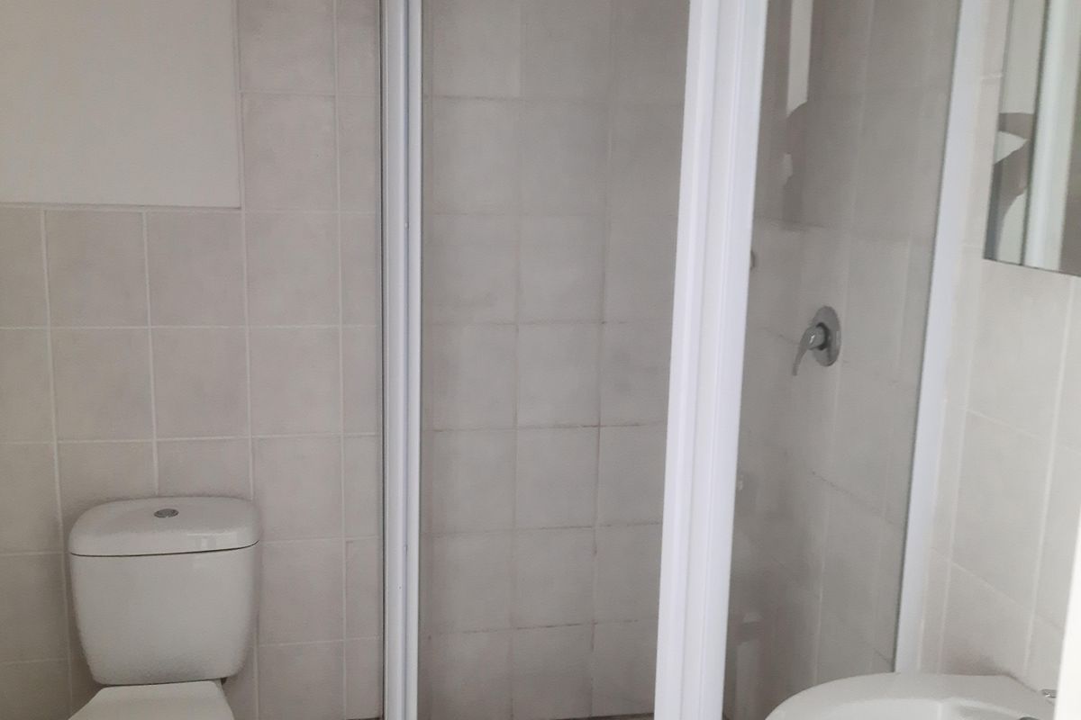 A functional bathroom featuring a corner shower enclosure, pedestal basin, and toilet with neutral wall and floor tiling.