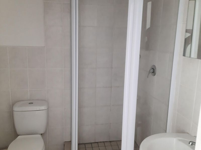 A functional bathroom featuring a corner shower enclosure, pedestal basin, and toilet with neutral wall and floor tiling.