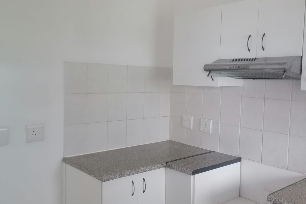 A compact, functional kitchen area featuring white built-in cabinetry, stone-look laminate countertops, a tiled backsplash, and an integrated extractor fan.