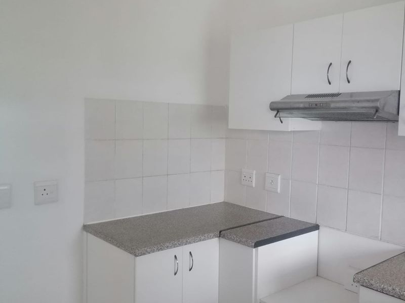 A compact, functional kitchen area featuring white built-in cabinetry, stone-look laminate countertops, a tiled backsplash, and an integrated extractor fan.