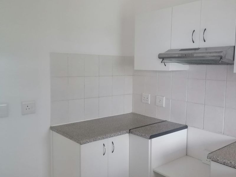A compact kitchen area featuring white built-in cabinetry, laminate countertops, a tiled backsplash, and an integrated extractor fan.