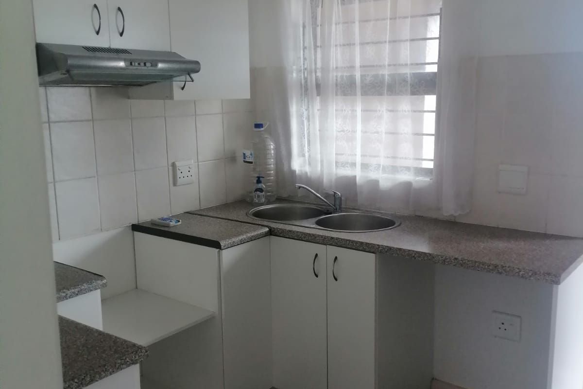 A functional kitchen featuring laminate countertops, a stainless steel double sink, built-in cabinetry, and an extractor fan with tiled splashback and flooring.