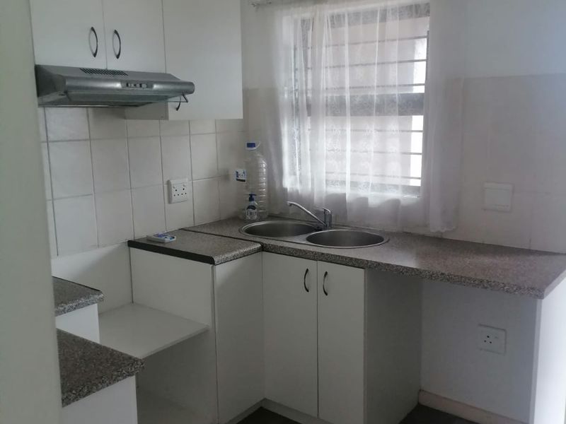 A functional kitchen featuring laminate countertops, a stainless steel double sink, built-in cabinetry, and an extractor fan with tiled splashback and flooring.