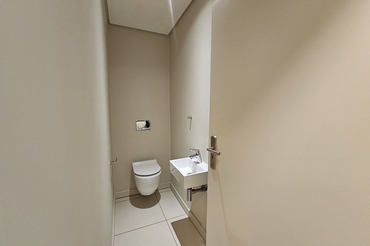 A compact guest bathroom featuring a wall-mounted toilet, a small basin with a chrome mixer tap, and neutral floor tiling.