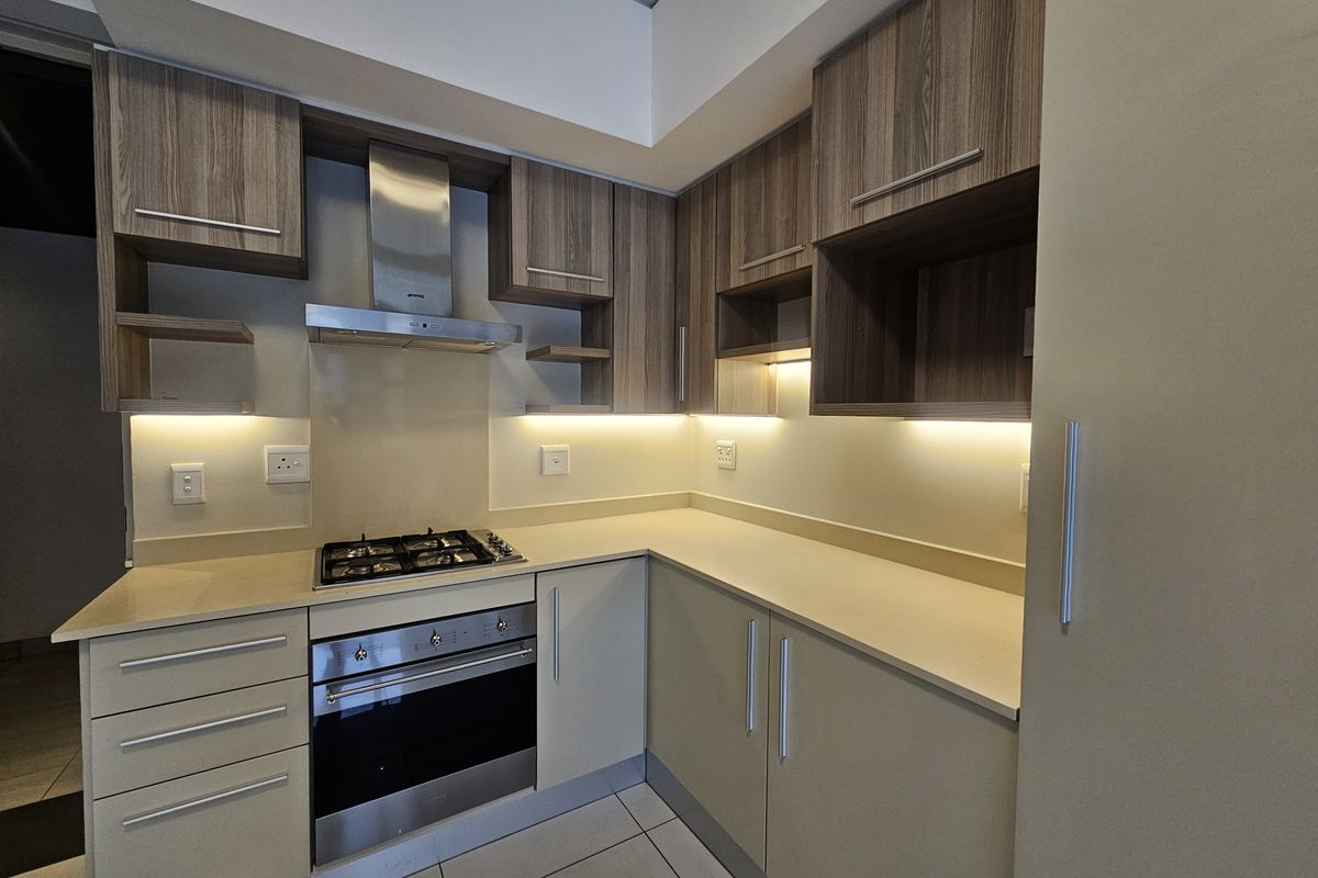 Modern kitchen featuring wood-grain cabinetry, stone countertops, built-in oven, gas hob, and stainless steel extractor fan with under-cabinet lighting.