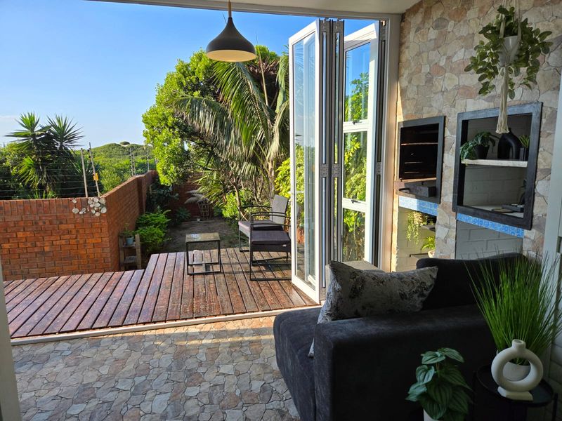 Covered patio featuring timber decking, stone-clad walls, a built-in braai, and folding stacking doors that open to a private garden area.