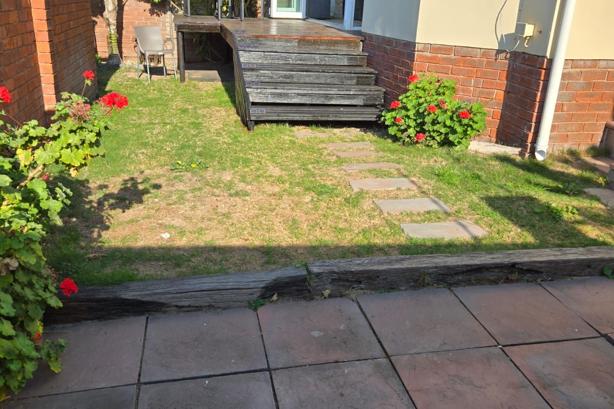 Rear exterior view of the townhouse featuring a timber deck, paved patio area, and a small garden with brick boundary walls.