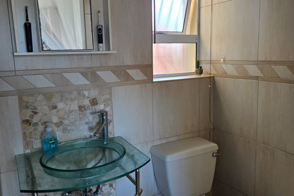 A compact bathroom featuring a glass vessel sink, chrome faucet, wall-mounted medicine cabinet, and ceramic toilet with neutral wall and floor tiling.