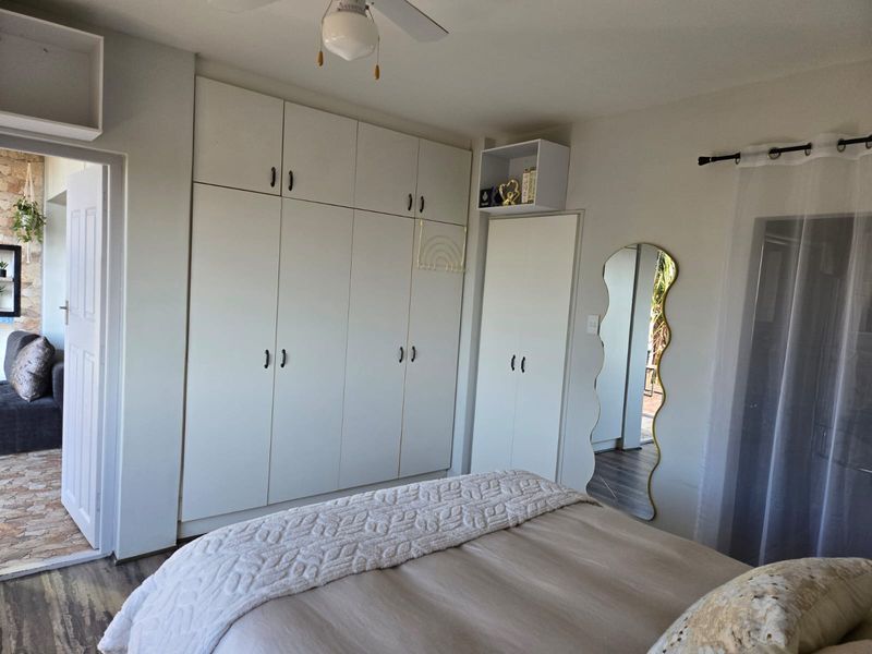 A well-maintained bedroom featuring extensive built-in cupboard storage, a ceiling fan, and durable laminate flooring with direct access to an outdoor area.