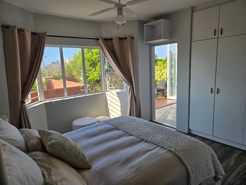 Bright bedroom featuring built-in cupboards, a ceiling fan, and a bay window with direct access to an outdoor patio area.
