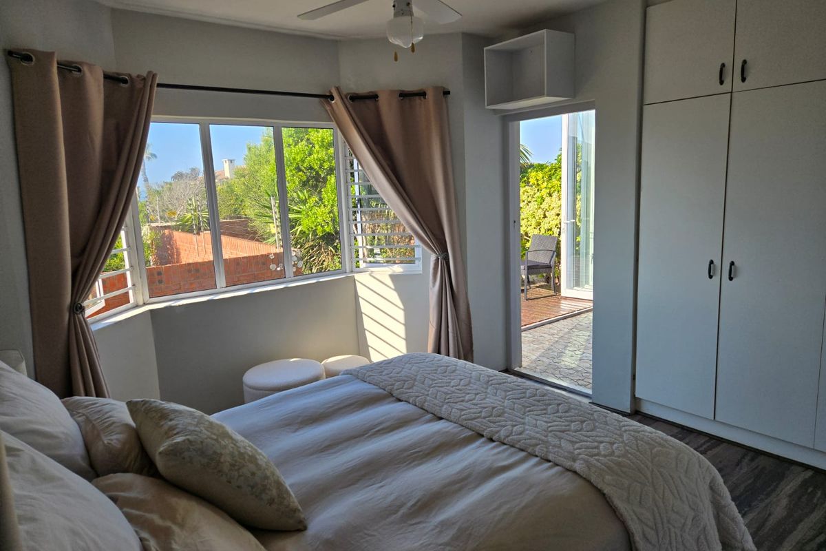 Bright bedroom featuring built-in cupboards, a ceiling fan, and a bay window with direct access to an outdoor patio area.