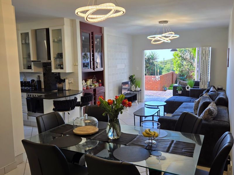 Spacious open-plan living, dining, and kitchen area featuring modern pendant lighting, tiled floors, and seamless access to an outdoor patio through sliding glass doors.