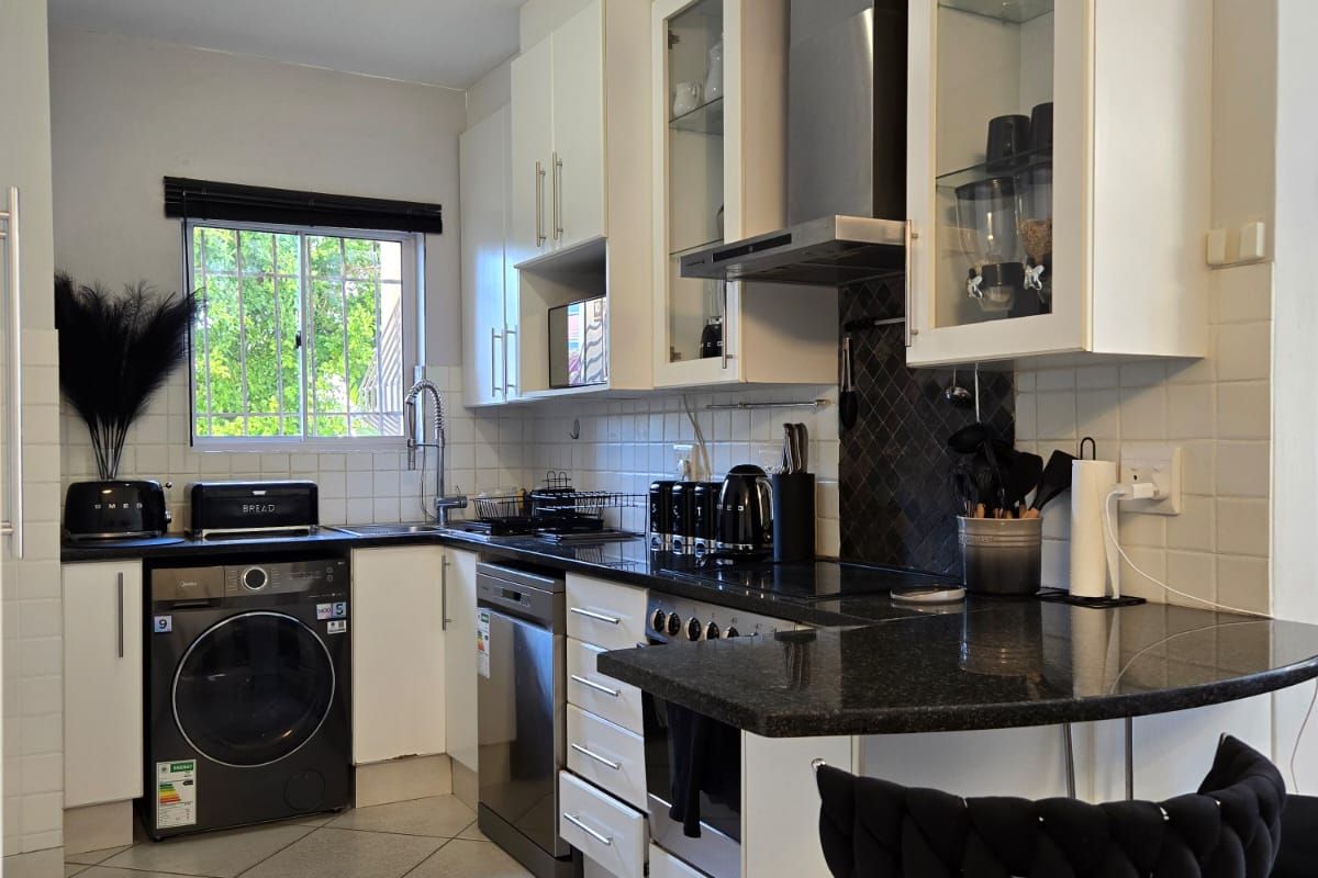 A functional kitchen featuring white cabinetry, dark granite countertops, tiled backsplash, built-in oven, extractor fan, and tiled flooring with a breakfast bar area.