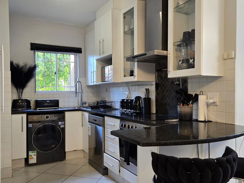 A functional kitchen featuring white cabinetry, dark granite countertops, tiled backsplash, built-in oven, extractor fan, and tiled flooring with a breakfast bar area.