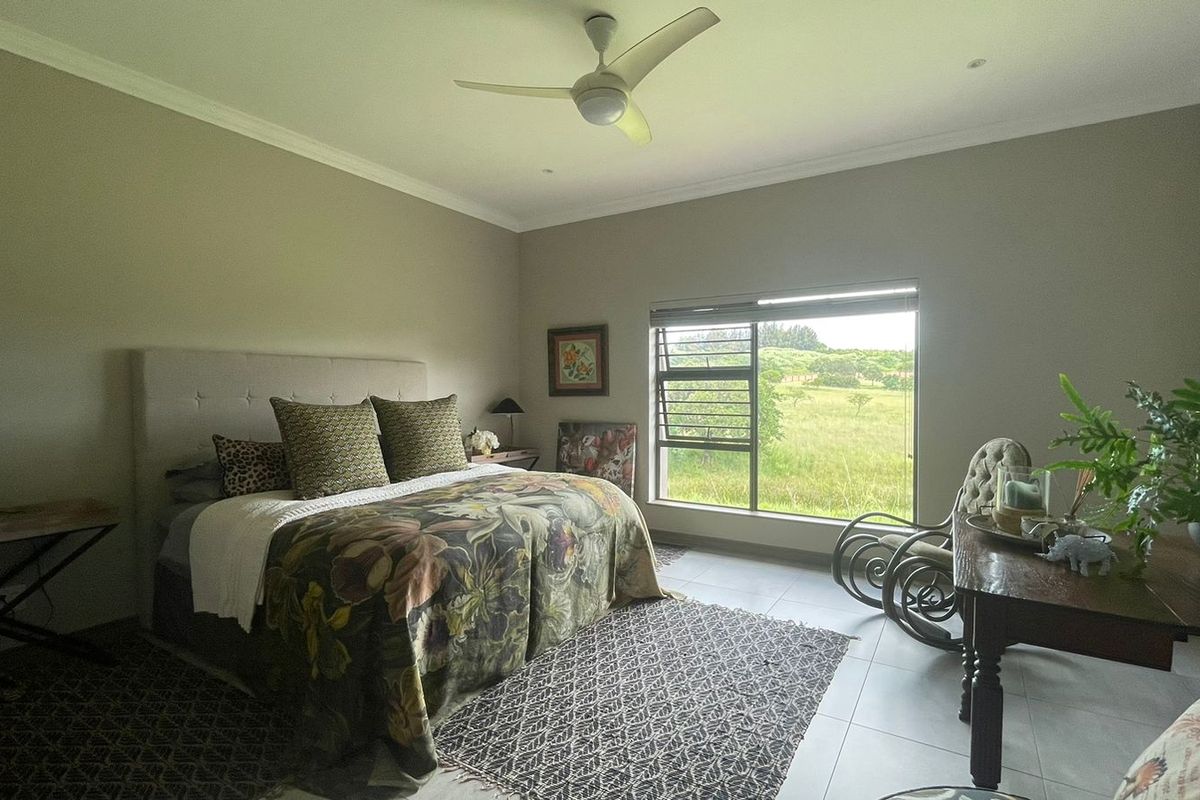 A spacious bedroom featuring tiled flooring, a ceiling fan, and a large window offering scenic views of the surrounding landscape.
