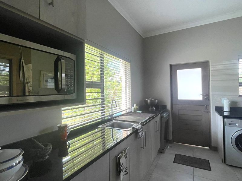 A functional scullery featuring granite countertops, built-in cabinetry, a stainless steel sink, and space for a washing machine with direct exterior access.
