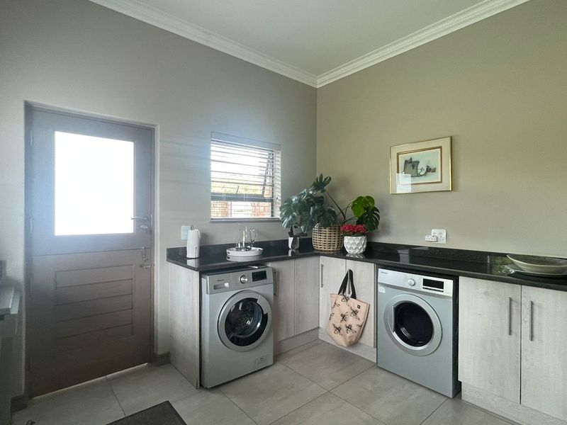 A functional laundry room featuring granite countertops, built-in cabinetry, tiled flooring, and direct access to the exterior.