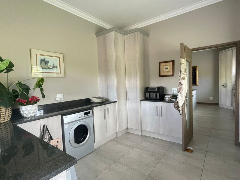 A functional laundry room featuring light wood-finish cabinetry, dark granite countertops, and neutral floor tiles, providing ample storage and workspace.