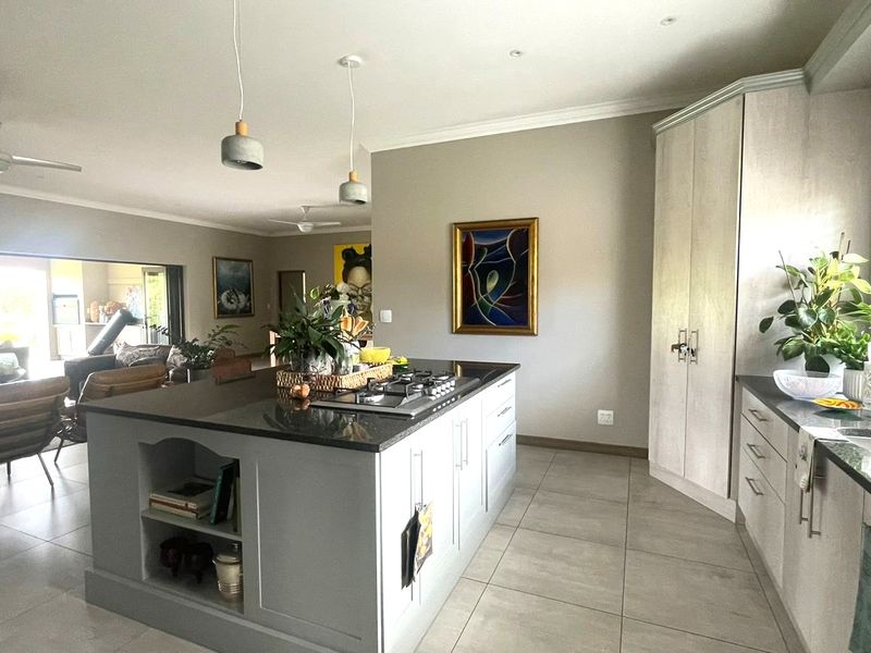 Spacious open-plan kitchen featuring a large central island with a gas hob, granite countertops, and ample built-in cabinetry, flowing into the living area.