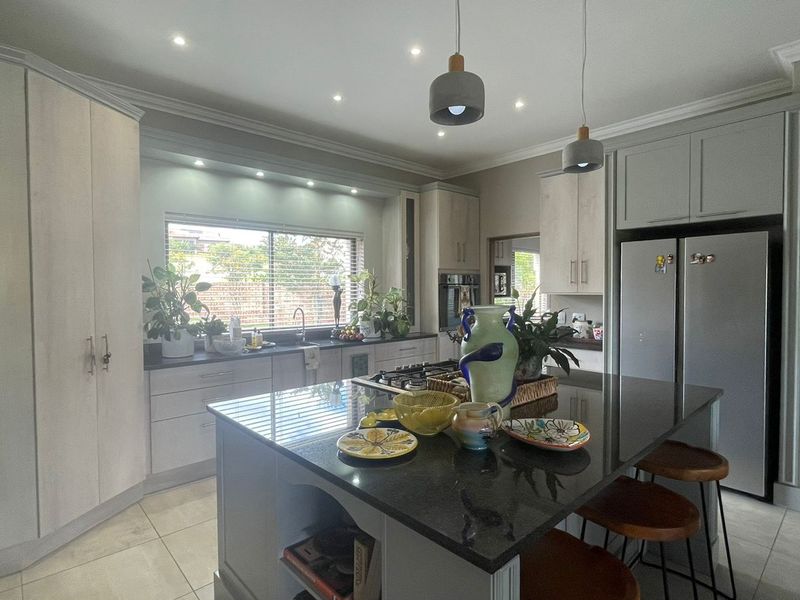 Modern kitchen featuring a central island with granite countertops, ample built-in cabinetry, gas hob, and stylish pendant lighting in a bright, open space.