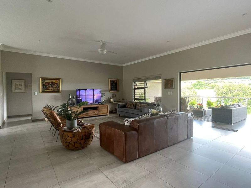 Spacious open-plan living area featuring neutral tiled flooring, recessed lighting, and seamless flow to an outdoor patio through large sliding glass doors.