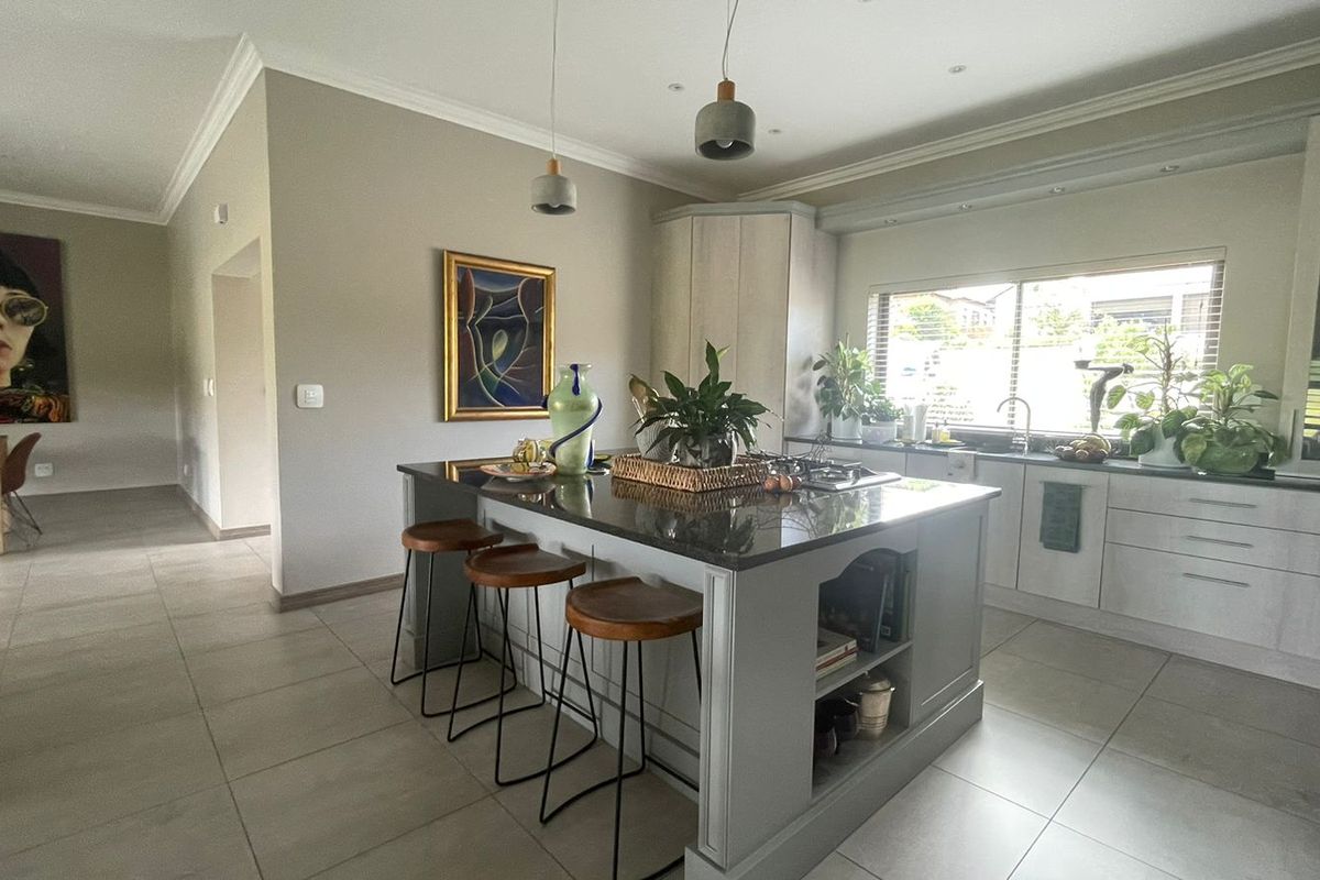 Modern kitchen featuring a central island with stone countertops, ample built-in cabinetry, tiled flooring, and stylish pendant lighting in an open-plan layout.