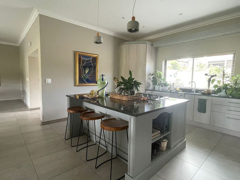 Modern kitchen featuring a central island with stone countertops, ample built-in cabinetry, tiled flooring, and stylish pendant lighting in an open-plan layout.