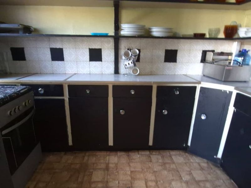 A functional kitchen featuring dark cabinetry, laminate countertops, tiled backsplash, and open shelving, offering potential for a modern renovation.