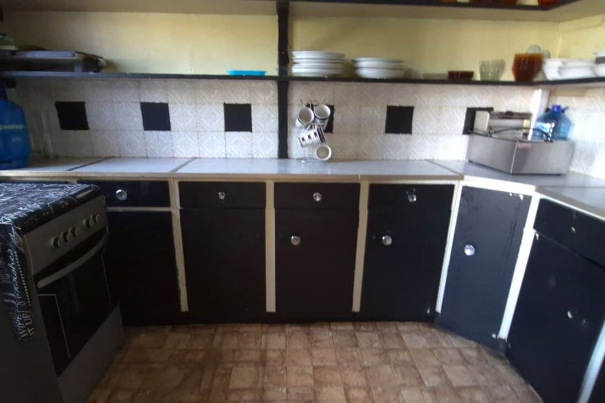 A functional kitchen featuring dark cabinetry, laminate countertops, tiled backsplash, and open shelving, offering potential for a modern renovation.