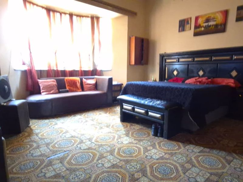 Spacious bedroom featuring a large bay window and patterned flooring, offering a comfortable layout with potential for modern updates.