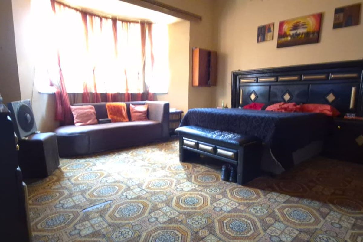 Spacious bedroom featuring a large bay window and patterned flooring, offering a comfortable layout with potential for modern updates.