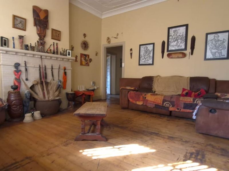Spacious living room featuring a classic brick fireplace, original hardwood flooring, and decorative ceiling molding, offering a warm and character-filled living space.