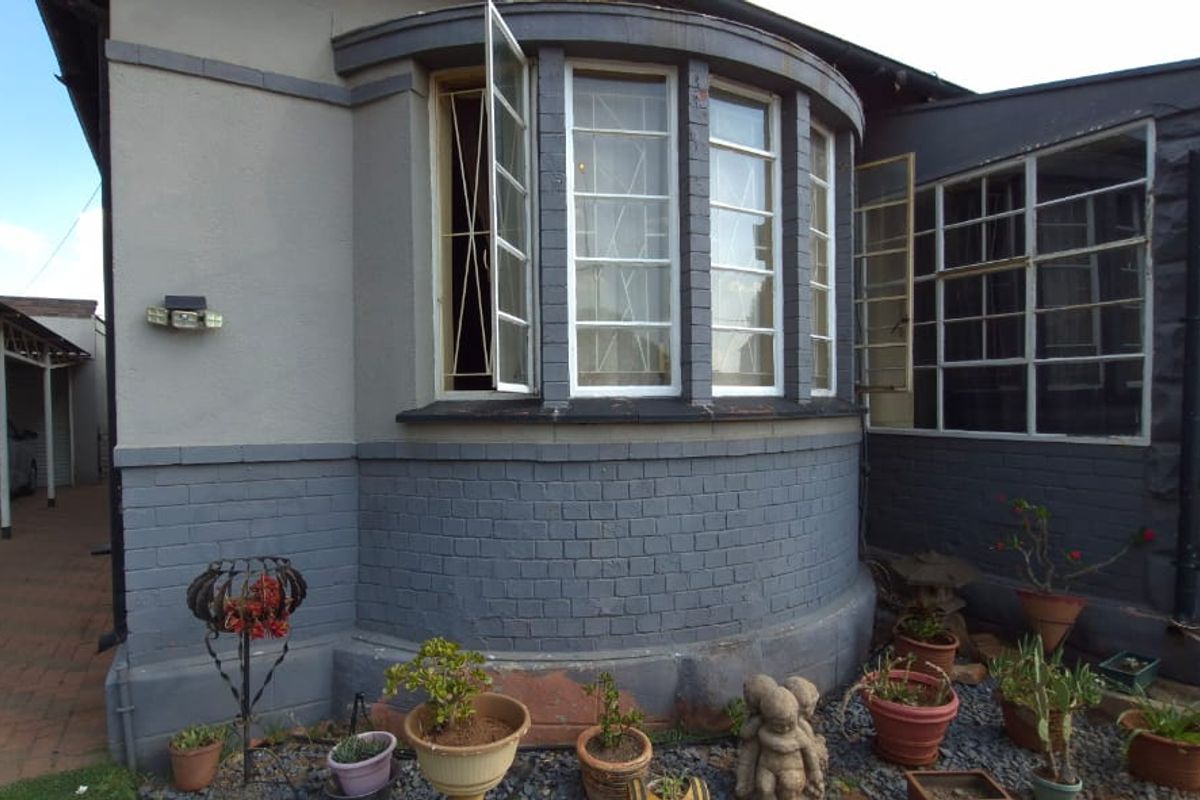 Rear exterior view of the property featuring a curved brick facade, steel-framed bay windows, and an attached carport.