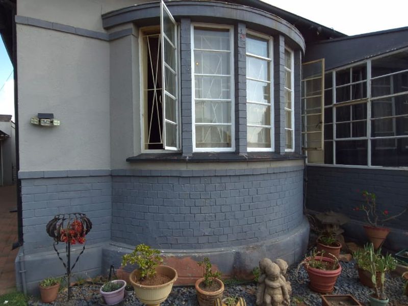 Rear exterior view of the property featuring a curved brick facade, steel-framed bay windows, and an attached carport.