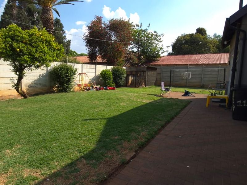 A spacious rear garden featuring a paved patio area, established lawn, and secure precast concrete boundary walls.