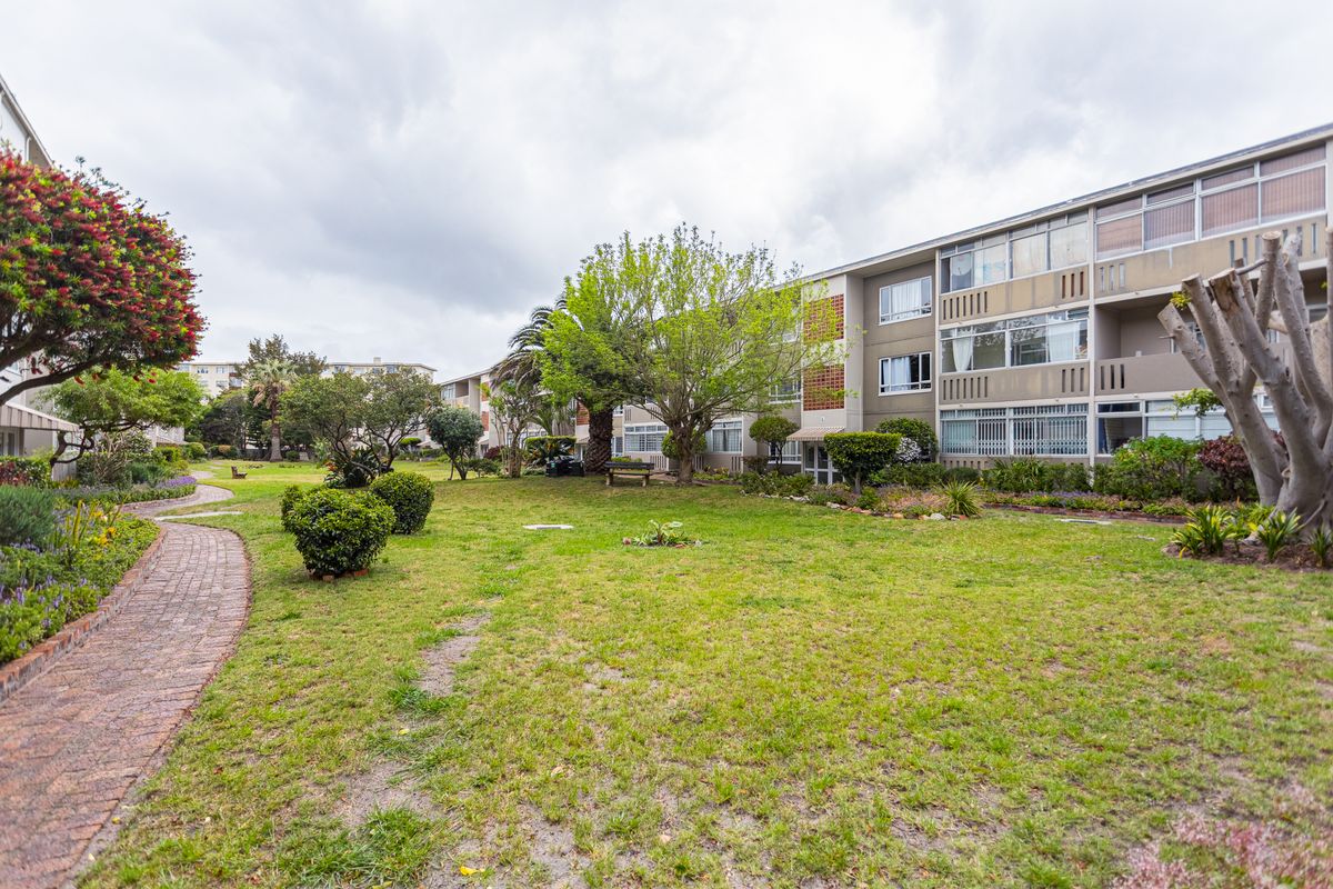 A view of the communal garden area featuring a brick pathway and established landscaping in front of the apartment building complex.