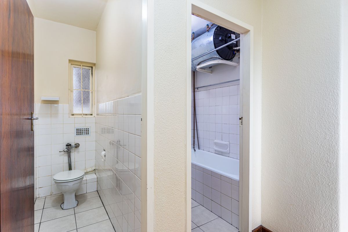 A functional bathroom featuring a separate toilet area and a bathtub with an exposed water heater unit.