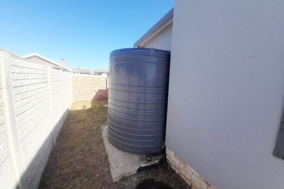 A side yard area featuring a large water storage tank mounted on a concrete plinth, enclosed by precast concrete and brick boundary walls.
