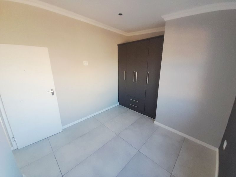 A clean, empty bedroom featuring neutral wall tones, modern large-format floor tiles, and dark built-in cupboards with integrated storage.
