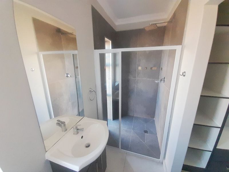 Modern bathroom featuring a vanity basin, large wall-mounted mirror, and a spacious walk-in shower with a rain shower head and sliding glass door.