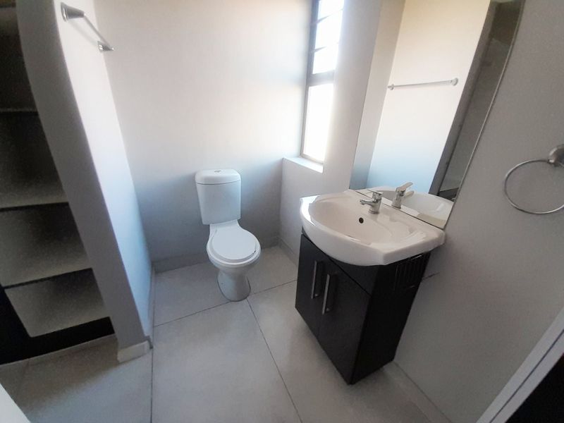 A clean, functional bathroom featuring a modern vanity with basin, a standard toilet, and built-in shelving, finished with neutral floor tiles.